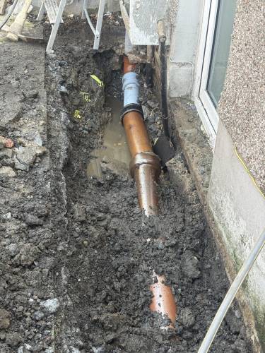 Excavated drain pipe repair beside a property